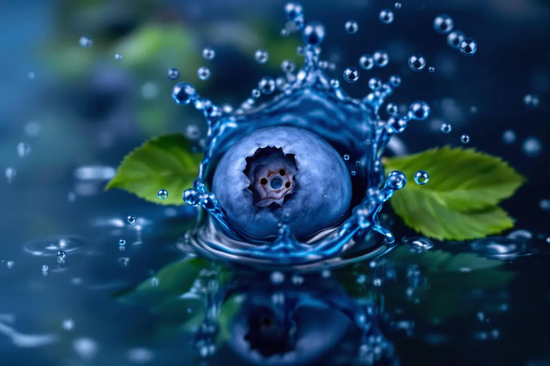 a close-up of a blueberry surrounded by a splash of dark blue water and tiny leaves and bubbles, across a blurred background