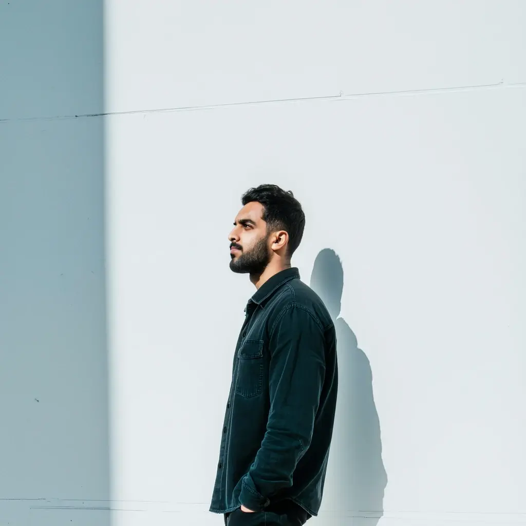 a portrait of a man standing in front of a white wall. His gaze is directed to the right, looking towards something beyond the frame