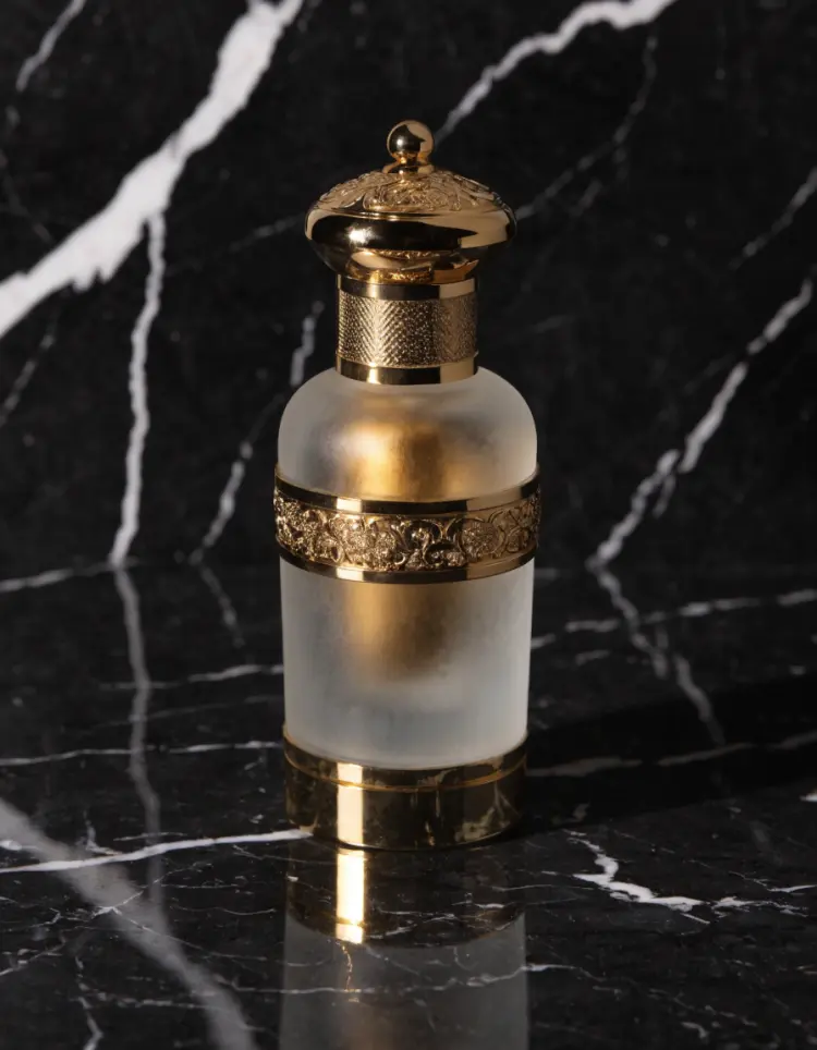 High-end product photography of a luxury perfume bottle on a polished black marble surface. The bottle is frosted glass with gold accents. Soft directional studio lighting with a single reflection streak. Minimal, premium, editorial beauty photography.