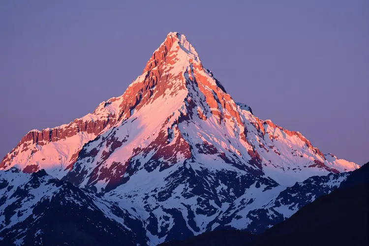 a majestic snow-capped mountain peak bathed in a warm glow of the setting sun