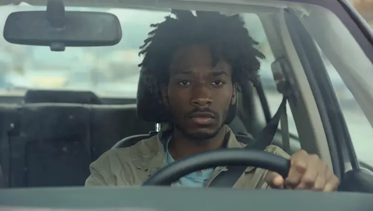 show me the man from @img_1 framed through the windshield of a car like the reference @img_2